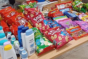 Tisch mit Snacks und Hygieneprodukten, darunter Chips, Süßigkeiten und Pflegeartikel.