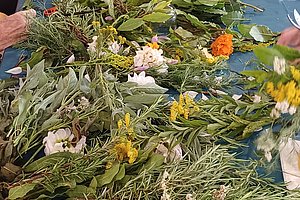 Mehrere Personen sitzen an einem Tisch und arrangieren frische Blumen und Pflanzen zu Sträußen