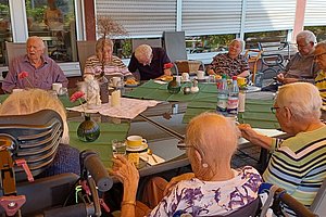 Ältere Menschen sitzen an einem Tisch im Freien, genießen Zeit miteinander bei Getränken und Snacks.