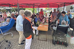 Gruppe älterer Menschen sitzt und steht unter einem roten Pavillon an einem langen Tisch im Freien