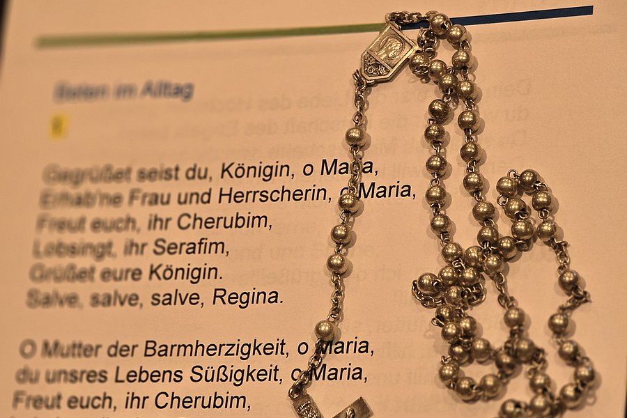 Silberner Rosenkranz mit Kreuz und glänzenden Perlen auf einem Textblatt von Marienhaus.