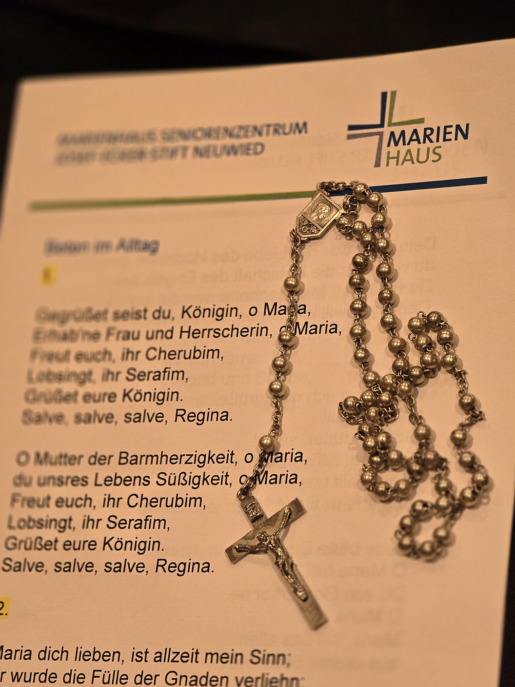 Silberner Rosenkranz mit Kreuz und glänzenden Perlen auf einem Textblatt von Marienhaus.