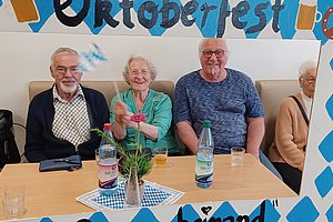 Gruppe älterer Menschen feiert Oktoberfest mit Getränken und Dekoration in einem fröhlichen Rahmen.