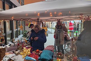 Marktstand mit einer Frau, die Waren inspiziert, umgeben von weihnachtlichen Dekorationen und Handarbeiten.