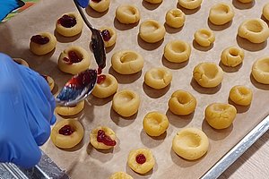 Plätzchen auf einem Blech werden von einer Person mit Marmelade befüllt