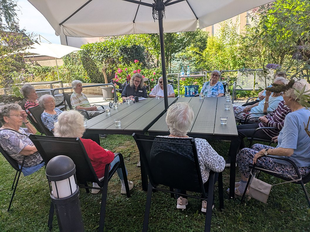 Gruppe älterer Menschen sitzt im Garten an einem großen Tisch unter einem Sonnenschirm