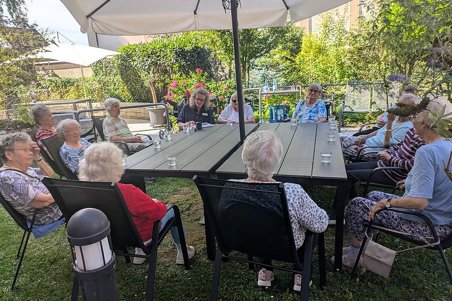 Gruppe älterer Menschen sitzt im Garten an einem großen Tisch unter einem Sonnenschirm