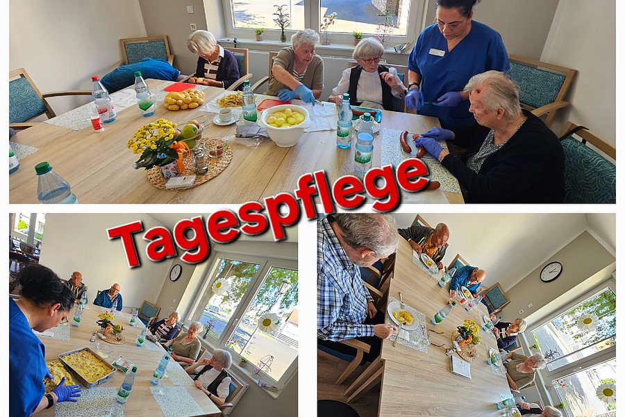 Mehrere ältere Menschen sitzen an einem großen Tisch in einem hellen Raum, eine Pflegekraft steht dabei, auf dem Tisch stehen Wasserflaschen und Obstschalen.