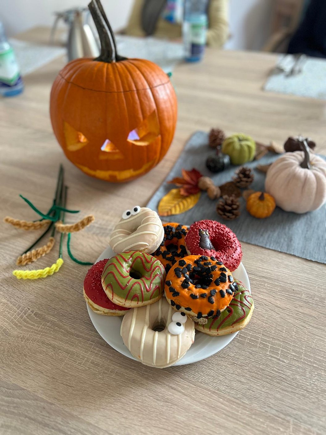 Herbstliche Deko mit bunten Halloween-Donuts und geschnitztem Kürbis auf einem Tisch.