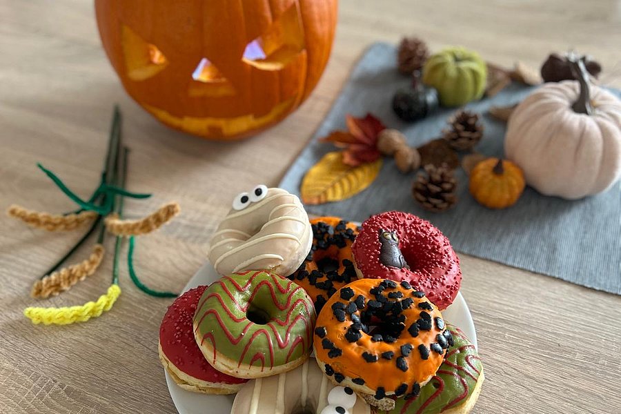 Herbstliche Deko mit bunten Halloween-Donuts und geschnitztem Kürbis auf einem Tisch.