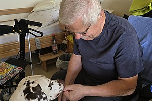 Älterer Mann sitzt auf einem Stuhl und hält die Pfote eines Dalmatiners in der Hand