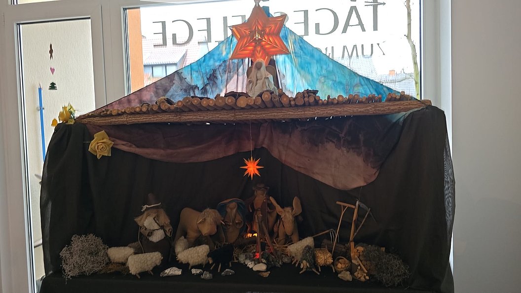 Krippe mit Stroh, Figuren und Adventsstern, dekorativ unter einem bunten Baldachin auf schwarzem Hintergrund.