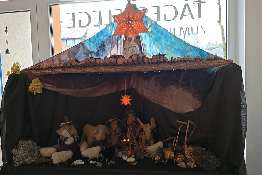 Krippe mit Stroh, Figuren und Adventsstern, dekorativ unter einem bunten Baldachin auf schwarzem Hintergrund.