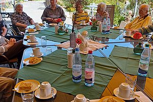 Gruppe älterer Menschen sitzt an einem großen Tisch im Freien und trinkt Kaffee