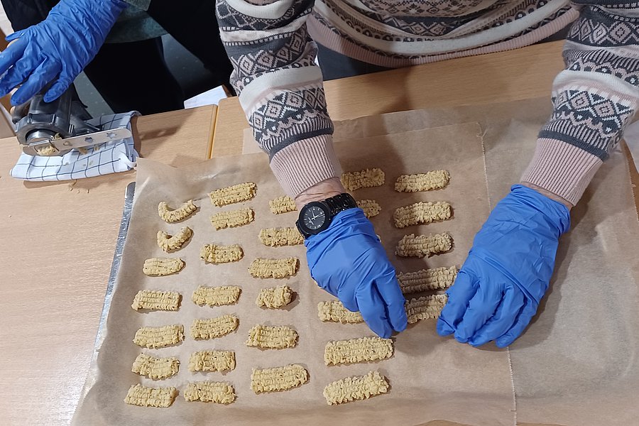 Hände mit blauen Handschuhen formen Snacks auf Backpapier für eine Backaktion.