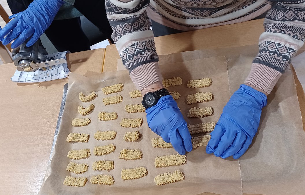 Hände mit blauen Handschuhen formen Snacks auf Backpapier für eine Backaktion.
