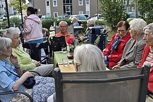 Gruppe älterer Menschen sitzt im Freien an einem Tisch und unterhält sich