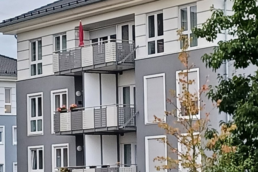 Mehrstöckiges Wohngebäude mit Balkonen, davor Parkbänke und ein kleiner Spielplatz mit buntem Bodenbelag.