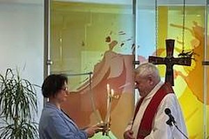 Zwei Personen in einer feierlichen Zeremonie mit einem Kreuz und Kerzen auf einem Altar.
