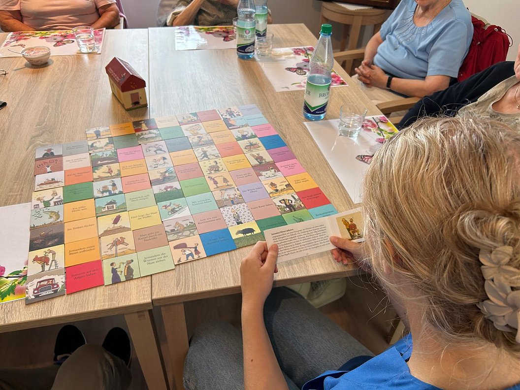 Mehrere Personen sitzen an einem Tisch und spielen ein buntes Brettspiel mit quadratischen Feldern