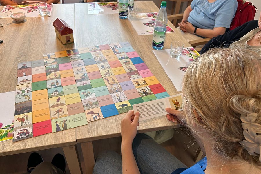 Mehrere Personen sitzen an einem Tisch und spielen ein buntes Brettspiel mit quadratischen Feldern