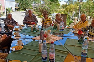 Gruppe älterer Menschen sitzt an einem großen Tisch im Freien und trinkt Kaffee