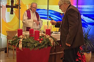 Feierliche Darstellung einer Adventsandacht mit zwei Personen, roten Kerzen und festlicher Dekoration.