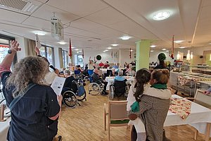 Einblicke in eine gesellige Versammlung mit älteren Menschen in einem Speisesaal, einige mit Programmen in der Hand.
