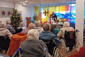 Senioren im Andachtsraum mit Weihnachtsbaum und festlicher Dekoration, Zelebration mit Kerzen und Musik.
