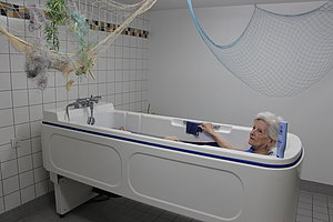 Eine Person entspannt in einer modernen Badewanne mit einem Pflegehilfsmittel im Badezimmer.