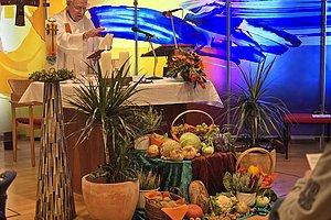 Festliche Erntedankdekoration mit Gemüse und Pflanzen vor einem Altar in einer kirchlichen Umgebung.