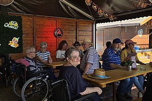 Gruppe von Menschen im Freien, die an einem Tisch sitzen, in einem gemütlichen Restaurant-Ambiente.