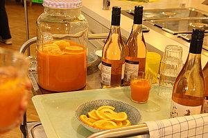 Glasbehälter mit Orangensaft und Orangenscheiben neben Flaschen und Gläsern auf einem Küchentisch