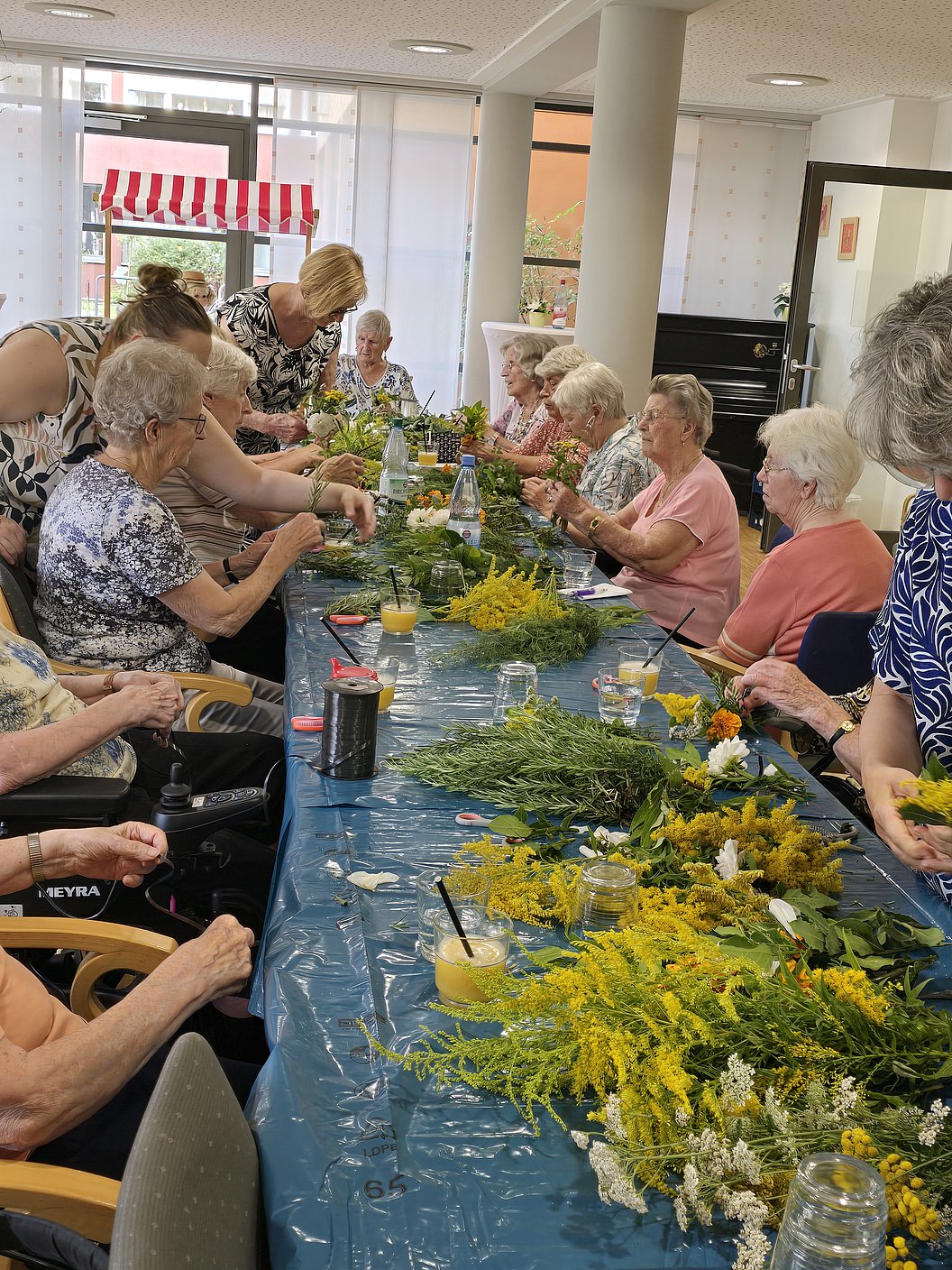 Gruppe älterer Menschen sitzt an einem langen Tisch und arrangiert Blumensträuße