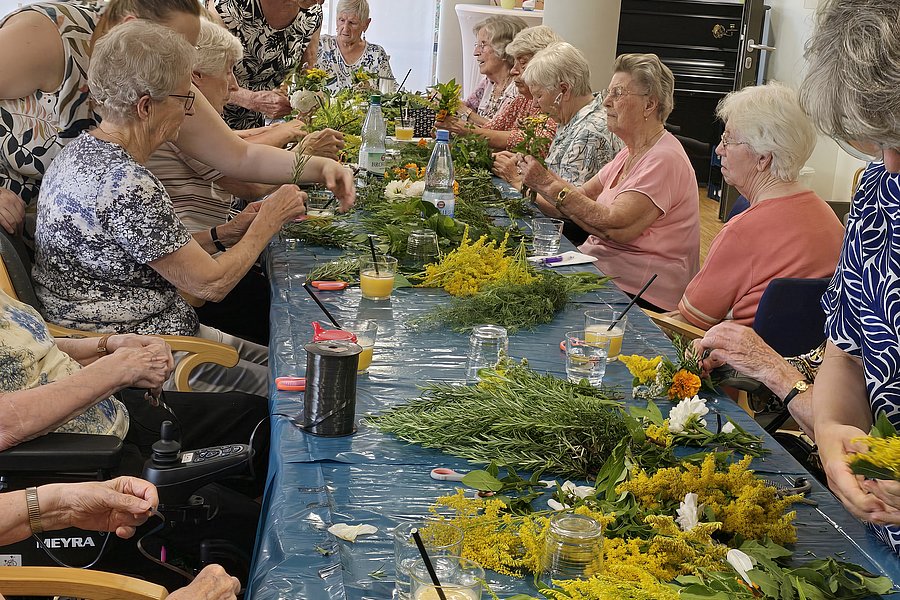 Gruppe älterer Menschen sitzt an einem langen Tisch und arrangiert Blumensträuße
