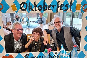 Oktoberfest-Rahmen mit drei fröhlichen Personen, die in einer festlichen Atmosphäre posieren.