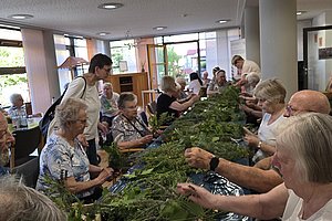 Seniorengruppe bei einer Bastelaktivität, die gemeinsam mit Pflanzenmaterialien arbeitet.