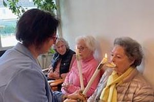 Gruppenbild, in dem eine Person mit Kerze eine andere Person anspricht, umgeben von weiteren älteren Damen.
