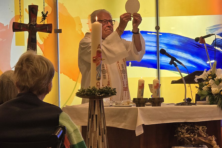 Priester hält Hostie während einer Messe vor einem Altar mit Kerzen und Kreuz