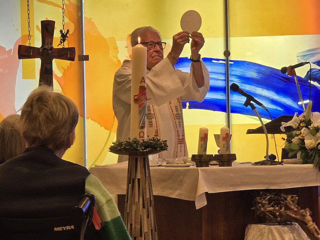 Priester hält Hostie während einer Messe vor einem Altar mit Kerzen und Kreuz