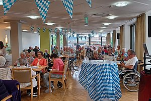Blick auf eine Seniorenveranstaltung mit Dekoration und vielen Gästen in einem hellen Raum.