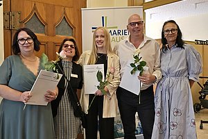 Gruppe von fünf Personen mit Urkunden und Blumen bei einer Veranstaltung