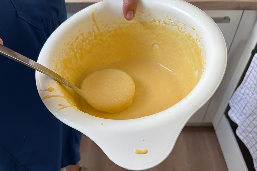 Hand hält eine weiße Schüssel mit gelbem Teig und einem Löffel darin