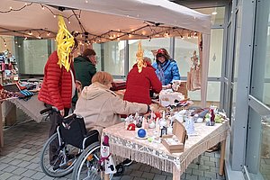Marktstand mit Besuchern, die handgemachte Produkte unter Zeltdach ansehen und kaufen.