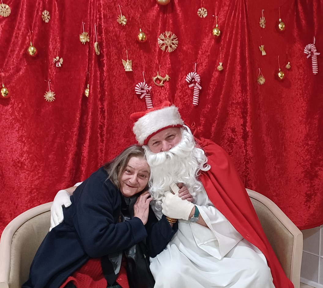 Frau und Weihnachtsmann auf einer Couch vor rotem Hintergrund mit Weihnachtsdeko.