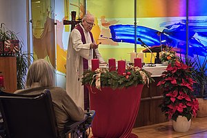 Gottesdienst mit einem Priester und Adventskranz in einer modernen Kirche.