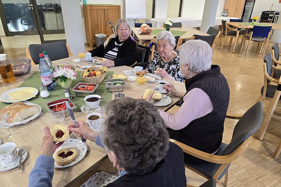 Mehrere ältere Menschen sitzen an einem Tisch und essen gemeinsam Kuchen und trinken Kaffee in einem hellen Raum