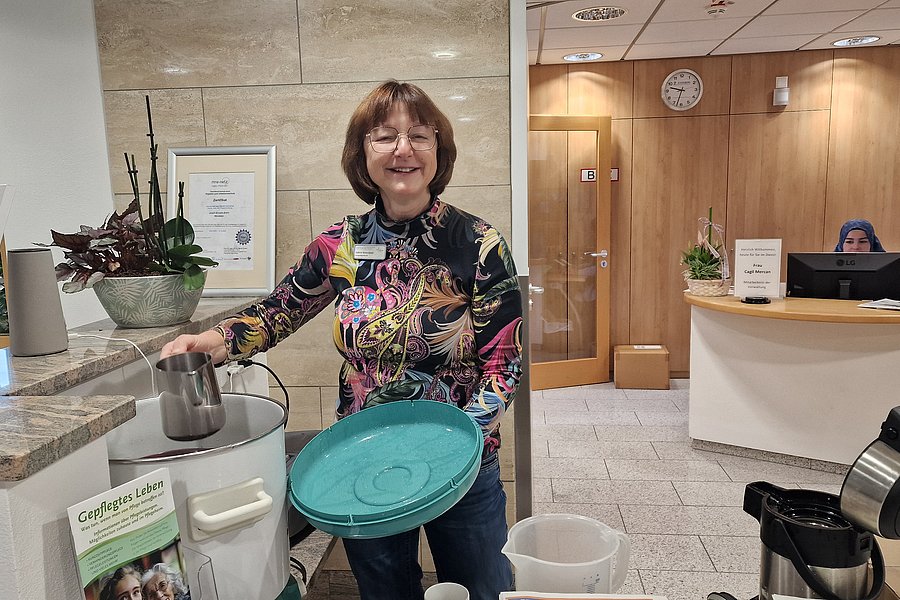 Frau mit buntem Shirt, die an einem Empfangstresen eine Kanne in eine grüne Schüssel schüttet.
