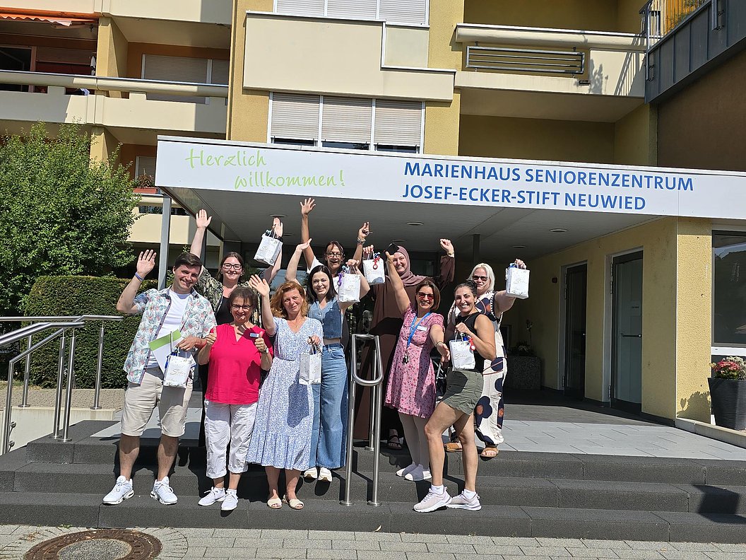 Gruppe von Menschen vor dem Eingang des Marienhaus Seniorenzentrums Josef-Ecker-Stift Neuwied winkt und hält kleine Tüten in der Hand