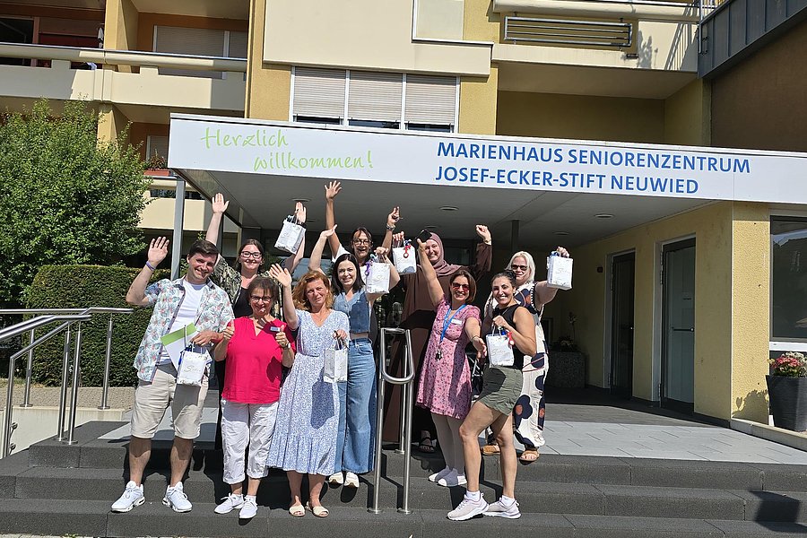 Gruppe von Menschen vor dem Eingang des Marienhaus Seniorenzentrums Josef-Ecker-Stift Neuwied winkt und hält kleine Tüten in der Hand
